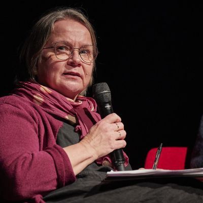 white woman with glasses, holding microphone